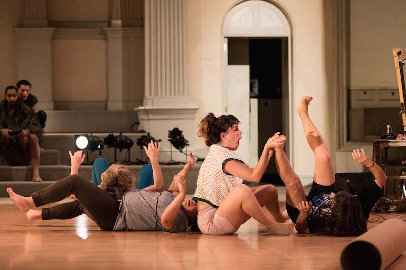 four dancers lay in various positions on the ground in a line